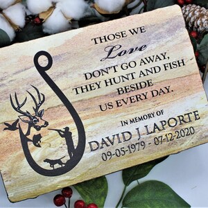 Peut inclure: Une plaque rectangulaire en pierre avec une texture naturelle en couches beige et marron. Elle pr&eacute;sente un motif noir en forme d'hame&ccedil;on contenant un cerf, un chasseur et un chien. Le texte indique : THOSE WE Love DON'T GO AWAY, THEY HUNT AND FISH BESIDE US EVERY DAY. IN MEMORY OF DAVID J LAPORTE 09-05-1979 - 07-12-2020.