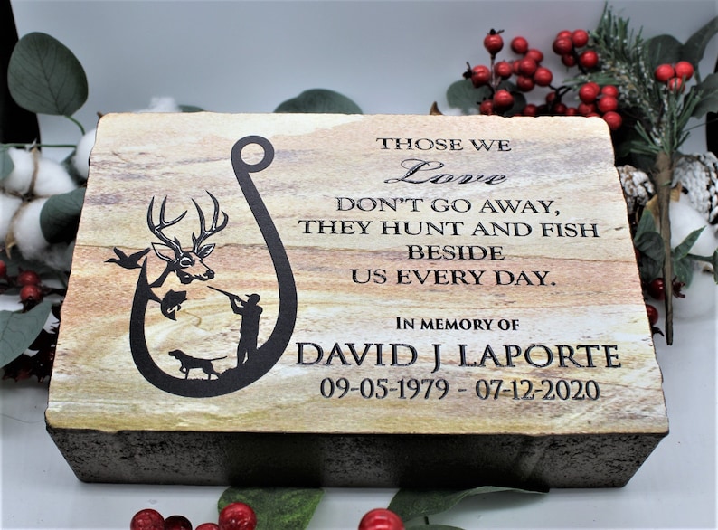 Peut inclure: Une plaque comm&eacute;morative rectangulaire en pierre avec une texture stratifi&eacute;e beige et brune. Elle pr&eacute;sente un motif grav&eacute; noir en forme d'hame&ccedil;on avec un cerf, un poisson, un chasseur et un chien. Le texte indique : THOSE WE Love DON'T GO AWAY, THEY HUNT AND FISH BESIDE US EVERY DAY. IN MEMORY OF DAVID J LAPORTE 09-05-1979 - 07-12-2020.