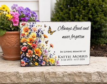 May include: A rectangular stone memorial plaque featuring a colorful floral arrangement of yellow, orange, pink, and blue flowers with two butterflies. The text reads: Always Loved and never forgotten, IN LOVING MEMORY OF KATTIE MORRIS 5-10-1975 - 4-17-2024.