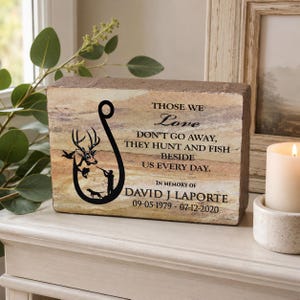 Peut inclure: Une plaque comm&eacute;morative rectangulaire en pierre avec un graphique noir repr&eacute;sentant un hame&ccedil;on, un cerf, un chasseur et un chien. Le texte indique : THOSE WE Love DON'T GO AWAY, THEY HUNT AND FISH BESIDE US EVERY DAY. IN MEMORY OF DAVID J LAPORTE 09-05-1979 - 07-12-2020.