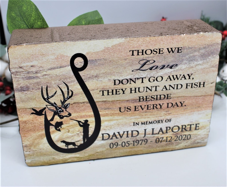 Peut inclure: Une plaque comm&eacute;morative rectangulaire en pierre avec une texture stratifi&eacute;e beige et brune. Elle pr&eacute;sente un graphique noir en forme d'hame&ccedil;on contenant un cerf, un poisson, un chasseur et un chien. Le texte indique : THOSE WE Love DON'T GO AWAY, THEY HUNT AND FISH BESIDE US EVERY DAY. IN MEMORY OF DAVID J LAPORTE 09-05-1979 - 07-12-2020.