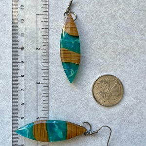 May include: A pair of teal and wood resin earrings with silver hooks. The earrings are shaped like a teardrop and have a wood grain pattern. The earrings are about 2 inches long.