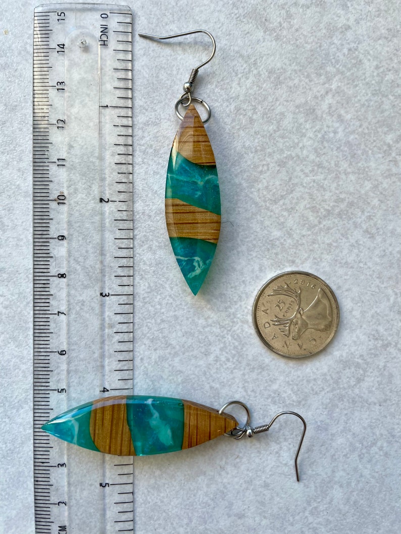May include: A pair of teal and wood resin earrings with silver hooks. The earrings are shaped like a teardrop and have a wood grain pattern. The earrings are about 2 inches long.