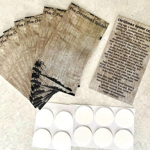 Puede incluir: Una colección de etiquetas de papel impresas con un diseño de vetas de madera, con el texto "The Christmas Spider" y una silueta negra de una palmera. También se incluyen pegatinas circulares blancas y una tarjeta impresa con una historia.