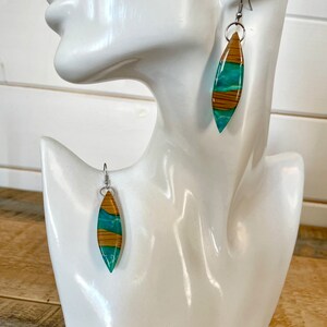 May include: A pair of dangle earrings with a teal and brown wood-like design. The earrings are made of resin and have silver hooks.