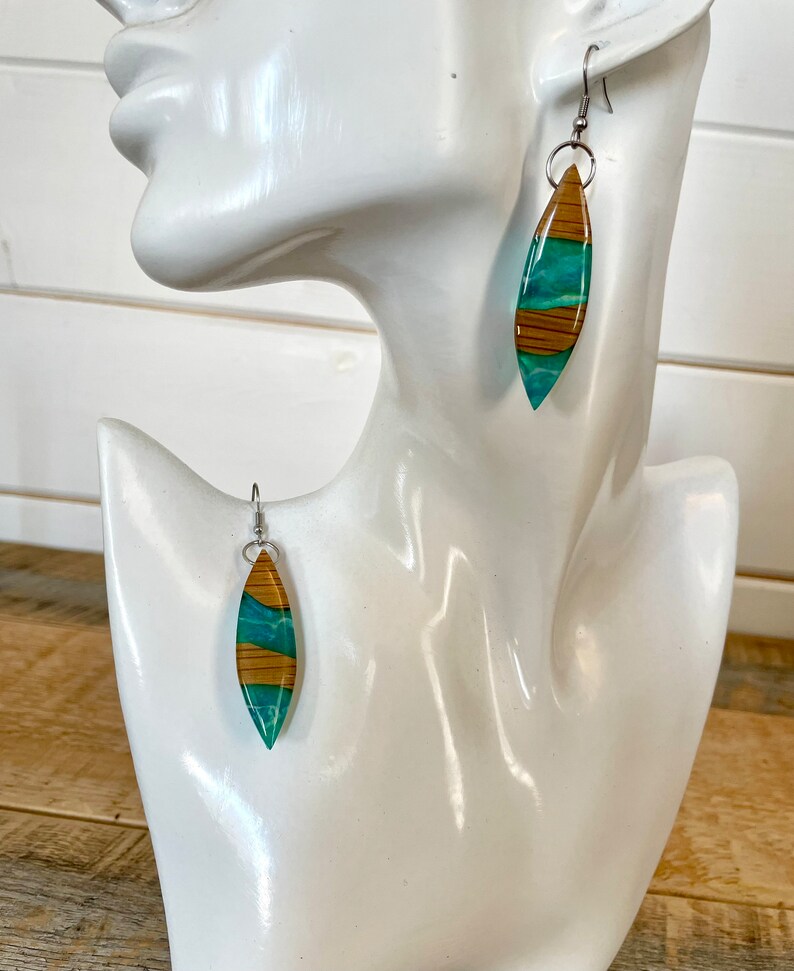 May include: A pair of dangle earrings with a teal and brown wood-like design. The earrings are made of resin and have silver hooks.