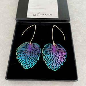 May include: A pair of iridescent leaf-shaped earrings with a gold hook. The earrings are in a black box with the text "L WOODS" on the lid.