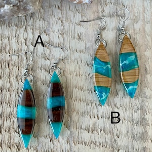 May include: Two pairs of earrings with turquoise and brown resin inlay. The earrings are shaped like a teardrop and have silver hooks.