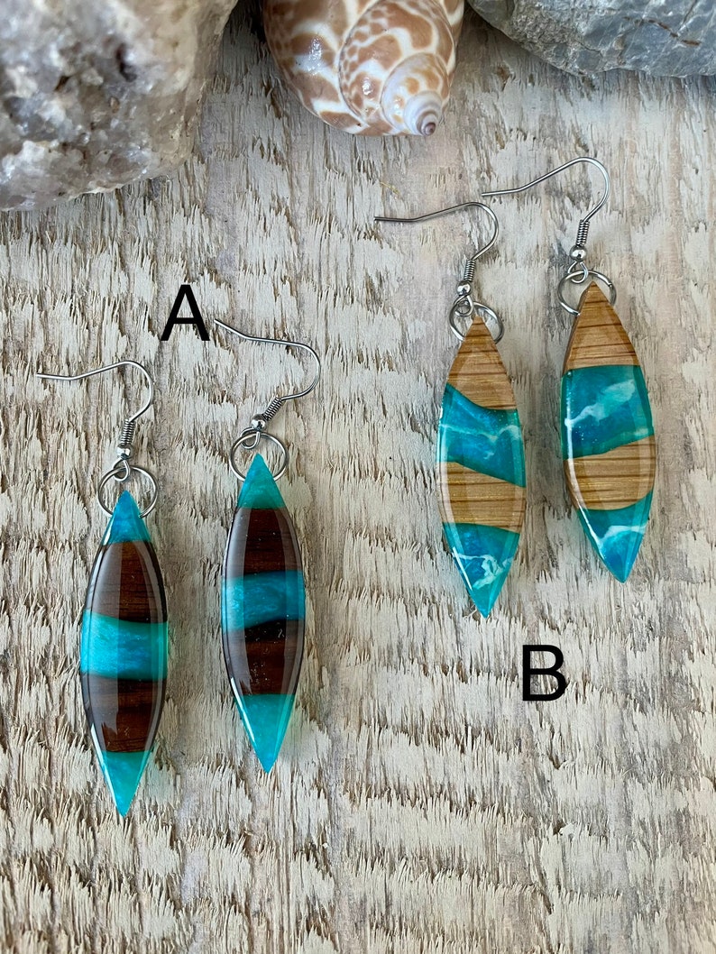 May include: Two pairs of earrings with turquoise and brown resin inlay. The earrings are shaped like a teardrop and have silver hooks.