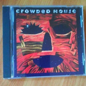 May include: A compact disc case with a red, yellow, and blue abstract design. The text "Crowded House" is printed in white on the front of the case.