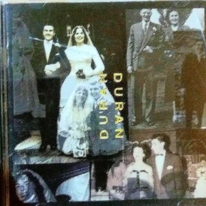 May include: A black and white photo of a wedding couple. The bride is wearing a white dress with a lace overlay and the groom is wearing a black suit. The photo is framed with a gold border and the word "DURAN DURAN" is printed in gold letters.