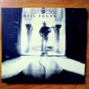 May include: Album cover for Neil Young's album, featuring a silhouette of a person playing a guitar in a doorway. The album title "NOISE" is at the top, with "NEIL YOUNG" below. The image has a dark, moody aesthetic.