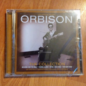 May include: A 2-CD special edition collection of Roy Orbison music. The cover features a black and white photo of Roy Orbison playing a guitar. The text on the cover reads "2CD Special Edition Roy Orbison The Collection Including: Only The Lonely, Running Scared, Crying, Blue Angel, and Many More 50 Digitally Remastered Original Recordings."