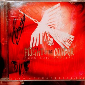 May include: A red CD case with a white stylized image of a condor with the text "Flight of the Condor" and "Jose Luis Madueño" printed on the front. The case has a clear plastic cover and a silver border.
