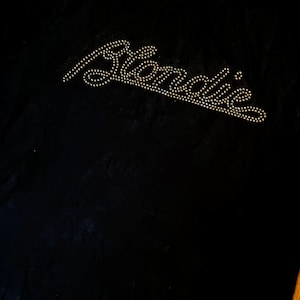 Op de afbeelding: Zwart T-shirt met de naam "Blondie" in strass-steentjes. De naam van de band staat ook kleiner bovenaan gedrukt. De stof heeft een licht getextureerde uitstraling.