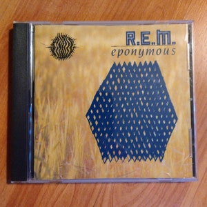 May include: A CD case with a yellow and blue design. The title of the album is "R.E.M. eponymous".