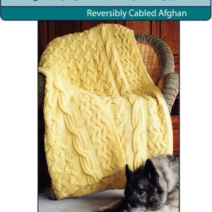 Könnte beinhalten: Ein gelber Zopfmuster-Afghan, der über einem Korbstuhl drapiert ist. Der Afghaner hat ein reversibles Zopfstrickmuster. Das Bild enthält den Text "Fiber Trends" und "Reversibly Cabled Afghan". Ein Hund liegt vor dem Stuhl auf dem Boden.