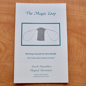 May include: A white pamphlet with the title "The Magic Loop" and a picture of a gray knitted fabric on two circular needles. The text below the image reads "Working Around On One Needle Knit socks and a whole lot more!" and "Sarah Hauschka's Magical Unvention written by Bev Galeskas published by Fiber Trends".