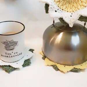 May include: A white enamel mug with a black rim and handle, featuring a corn graphic and the text "You're a-maize-ing." The mug sits on a white and green crocheted coaster. A stainless steel kettle rests on a yellow, white, and green crocheted coaster.