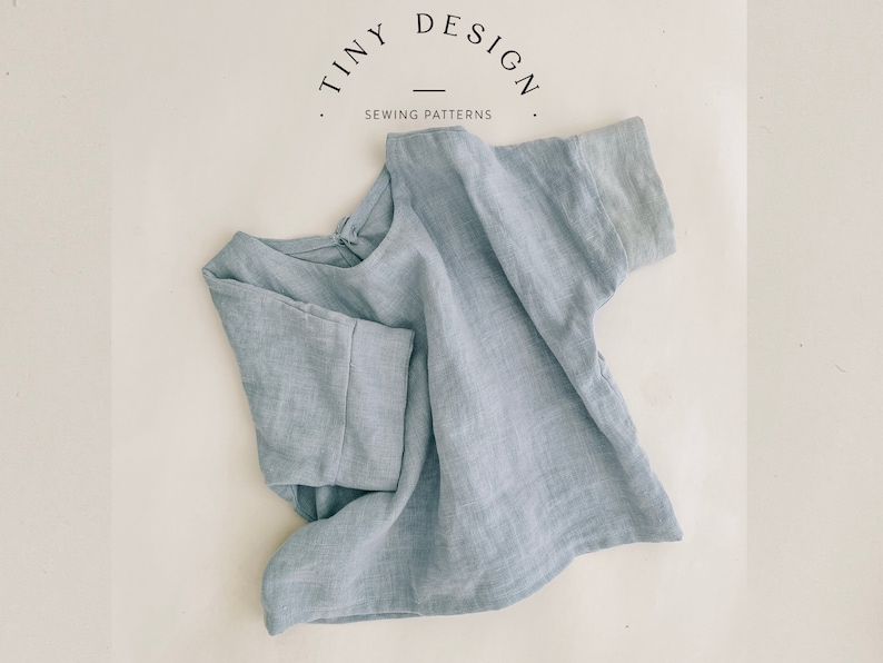 May include: A light blue linen top with short sleeves. The top is folded and laid flat on a white surface. The text "TINY DESIGN SEWING PATTERNS" is visible in the top left corner of the image.