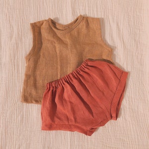 Puede incluir: Un conjunto de dos piezas para bebé con un top de lino sin mangas de color marrón claro y un pantalón corto de lino rojo.