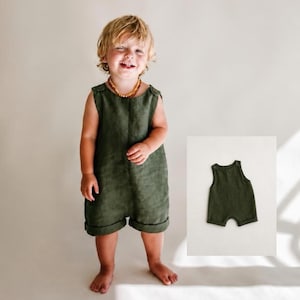 Puede incluir: Un pelele de color verde oliva sin mangas con cuello redondo y aberturas en las piernas con dobladillo. La prenda presenta un diseño sencillo de una sola pieza con silueta recta, mostrado tanto en un niño como producto independiente.