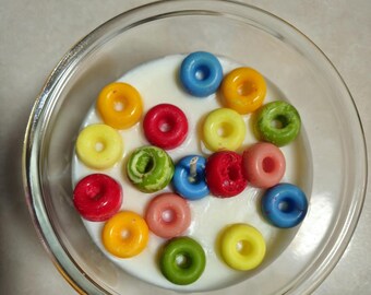 May include: A white candle with a variety of colorful donut-shaped wax decorations. The candle is in a clear glass jar.