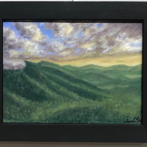 May include: A framed painting of a mountain landscape with a cloudy sky. The mountains are green and the sky is blue with white clouds. The painting is signed in the bottom right corner.