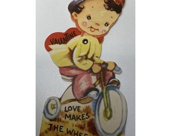 Tarjeta de San Valentín vintage de los años 40: Chica mecánica montando en bicicleta: El amor hace girar las ruedas.