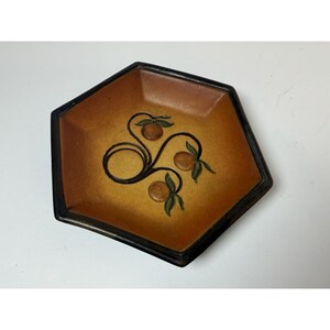 May include: A hexagonal decorative dish with a brown and yellow gradient. The dish features a black border and a painted design of oranges and leaves. The design is centered on the dish.