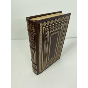 May include: A hardcover book with a dark brown leather cover and gold-colored decorative accents. The book's spine and cover feature intricate gold patterns and the title "Go Down in Darkness" by William Styron.
