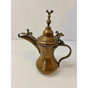 May include: A vintage brass coffee pot with a bulbous body, a long spout, and a curved handle. The pot is adorned with decorative bird-shaped accents and a tall, ornate finial. The metal has a warm, aged patina.