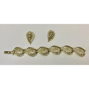 May include: A gold-toned jewelry set featuring a bracelet and matching earrings. The bracelet is composed of leaf-shaped links, and the earrings have a similar design. The set is displayed on a white surface.