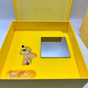 May include: A yellow box with a crystal figurine of a bear inside. The box is open and the bear is sitting on a yellow base. The box has the word "SWAROVSKI" printed on the inside of the lid.