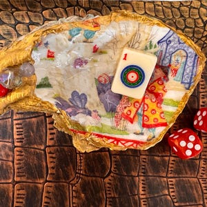 May include: An ornate oyster shell with gold edging, containing a Mahjong tile and red dice. The shell's interior is decorated with a colourful, illustrated scene. The dice are red with white spots, and the Mahjong tile shows the number 1 and a circular design.