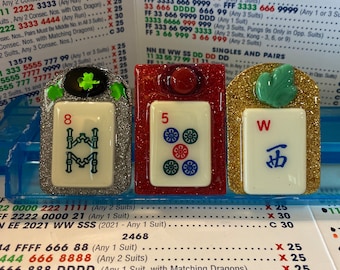 Könnte beinhalten: Drei dekorative Mahjong-Steine. Der erste Stein hat die Zahl 8 und ein grünes Kleeblatt. Der zweite Stein hat die Zahl 5 und rote Akzente. Der dritte Stein hat das chinesische Schriftzeichen für West.