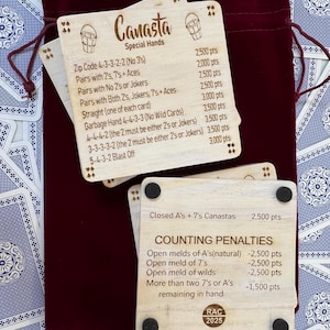 May include: Wooden Canasta game score cards with special hands and counting penalties printed on them. The cards are light brown with black text and are displayed with a burgundy velvet bag and a deck of playing cards.