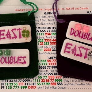 May include: Four small velvet pouches in red, green, purple, and pink, each containing white rectangular game pieces with the words "DOUBLES" and "EAST" in purple. The pouches have drawstrings.
