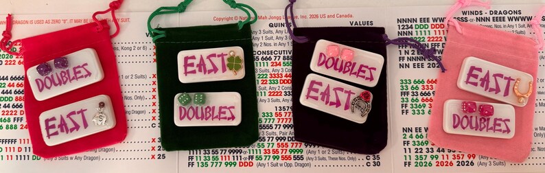 May include: Four small velvet pouches in red, green, purple, and pink, each containing white rectangular game pieces with the words "DOUBLES" and "EAST" in purple. The pouches have drawstrings.
