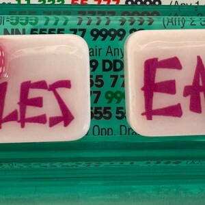 May include: Two rectangular trays with the words "DOUBLES" and "EAST" in magenta lettering. One tray has two red dice with white dots. The other tray has a gold horseshoe charm with a pearl.
