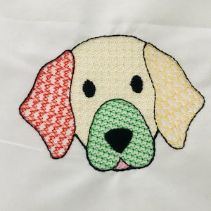 以下が含まれることがあります： クリーム色の頭、黒い目、緑色の鼻を持つ刺繍された犬の顔。耳は赤と黄色で模様が入っています。犬は白い背景に設定されています。