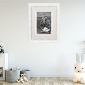 May include: A black and white framed photograph of a duck with its head tucked under its wing. The duck is standing in a shallow body of water.