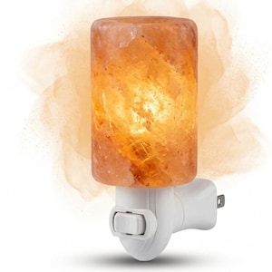 Peut inclure: Une veilleuse cylindrique en sel de l'Himalaya diffusant une lueur orange chaude, avec une texture cristalline naturelle. La lampe est montée sur une base enfichable en plastique blanc dotée d'un petit interrupteur à bascule frontal.
