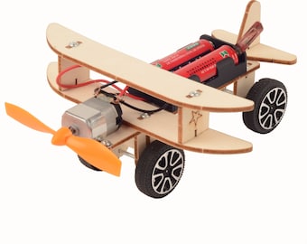 May include: A wooden toy airplane with a propeller, two wheels, and a battery compartment. The airplane is painted in natural wood tones and has a red battery pack.