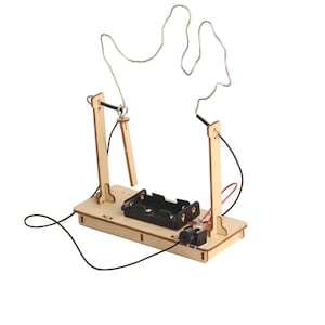 Op de afbeelding: Een houten handheld spel met een metalen draad in de vorm van een hand. Het spel heeft twee houten palen, een batterijhouder en een kleine zwarte luidspreker. De draadlus moet zonder aanraking worden geleid.
