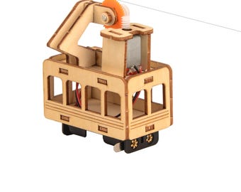 May include: A wooden toy model of a cable car with a small motor and a gear system. The cable car is painted in a light wood color and has a small orange gear on the top.