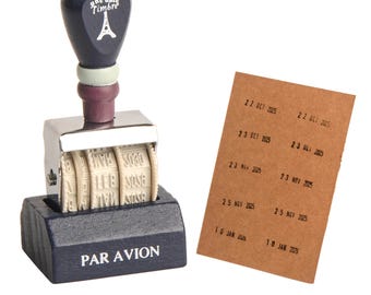 May include: A navy blue date stamp with the text "une date Timbre" and an Eiffel Tower illustration. The stamp is next to a brown paper with stamped dates, including "22 OCT 2025" and "23 OCT 2025". The base of the stamp reads "PAR AVION".