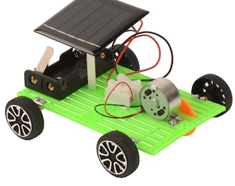 May include: A green and black toy car powered by a solar panel. The car has four black wheels with a white spoke design. The solar panel is black and has a grid pattern. The car has a small motor and a battery compartment.