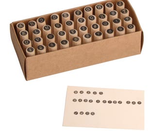 May include: A set of wooden letter and number stamps in a cardboard box. The stamps are arranged in rows and columns. A card below shows stamped text that reads "HAPPY ANNIVERSARY DAY" and "JACK".