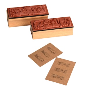 May include: Two rectangular rubber stamps with detailed designs sit on wooden blocks. The stamps are brown with intricate patterns, and the blocks are a light tan colour. Below are two small brown cards with stamped images.